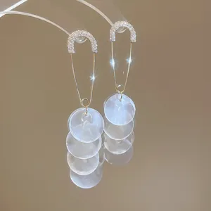 Dettaglio di eleganti orecchini a spilla dorati con pendenti in conchiglia bianca.