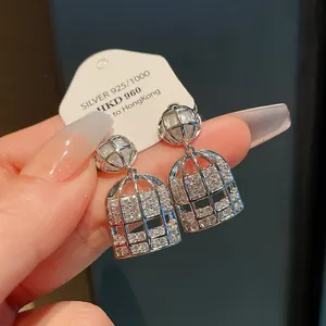 Primer plano de pendientes de jaula de plata con circonitas y perlas