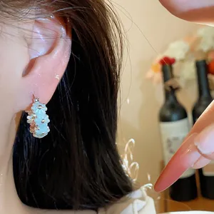 Macro detail of a light blue oil-drop flower hoop earring worn on a model's ear lobe