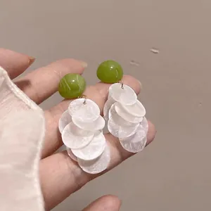 Macro view of French style drop earrings with green beads and white translucent discs.