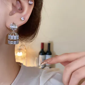 Primer plano de elegantes pendientes de plata en forma de jaula con circonitas en la oreja