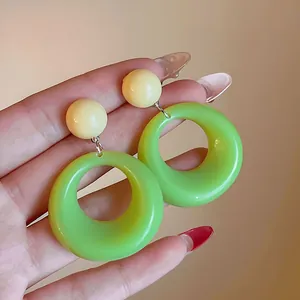 Detailed view of vibrant lime green acrylic hoop earrings held in hand for scale