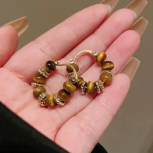 Close-up of gold-plated tiger eye stone hoop earrings in a hand for elegant Maillard style