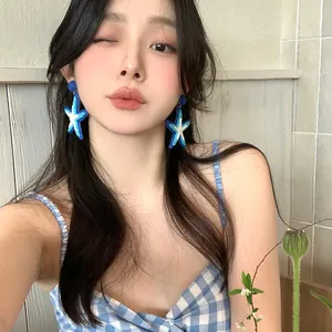 Blue woven star drop earrings with silver needle shown on an Asian model detail view