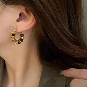 Close-up detail of tiger eye stone hoop earrings with gold-plated beads on a model.