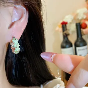 Detail view of sweet pale green enamel flower hoop earring worn on a model's ear.