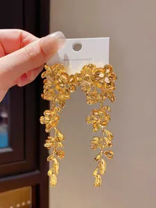 Primo piano di orecchini dorati con fiori e nappe di foglie su cartoncino
