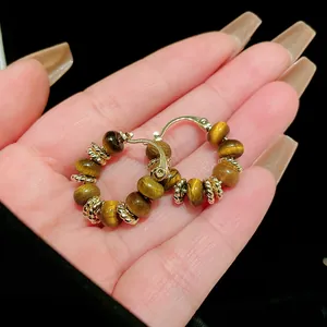 Detailed macro view of high-quality gold-plated tiger eye stone beaded hoop earrings on hand
