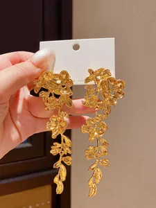 Primo piano di orecchini pendenti dorati a forma di fiori e foglie con nappe.