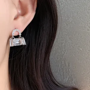 Close-up detail of silver handbag-shaped earring with clear crystals worn by model