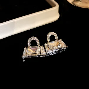 Close-up of silver handbag-shaped stud earrings encrusted with sparkling crystals