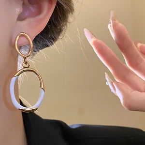 Detailaufnahme von goldenen ovalen Ohrhängern mit weißem Emaille-Finish im Vintage-Stil