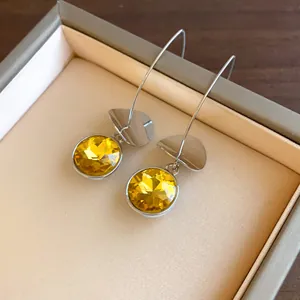 Dettaglio delle pietre gialle sfaccettate e placche metalliche su orecchini argento.