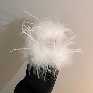 Close-up detail of fluffy white ostrich feather hair claw clip on black fabric background.