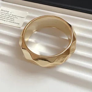 Detailed view of a gold-colored acrylic bangle featuring a modern geometric faceted design