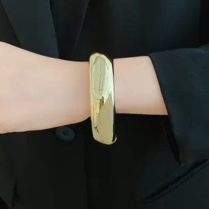 Close-up of a chunky geometric gold acrylic bangle worn by a model in a black blazer suit