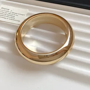 Close-up of a chunky gold-toned acrylic geometric bangle with a polished finish.