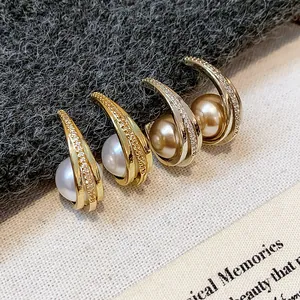 Macro di eleganti orecchini a perno con perle e zirconi stile francese su tessuto grigio testurizzato.