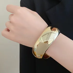Close-up of a chunky gold-tone geometric cuff bracelet on a model's wrist
