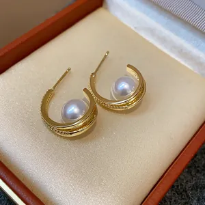 Dettaglio di eleganti orecchini a C dorati con perla centrale e pietre di zircone pavé
