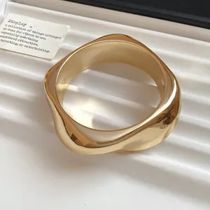 Close-up view of gold geometric acrylic bangle featuring a wavy irregular faceted design