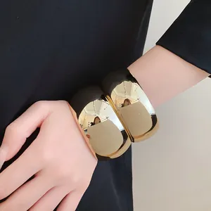 Close-up shot of chunky gold and black acrylic geometric cuff bangles worn on a wrist