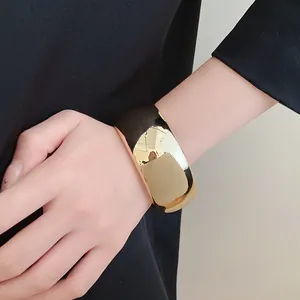 Detailed view of a wide gold-tone geometric cuff bracelet worn on a wrist.