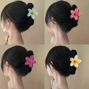 Detail view of multi-colored gradient frangipani flower hair claw clips worn on a bun