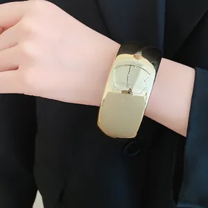 Close-up of a bold gold-tone geometric acrylic cuff bracelet worn over a black suit jacket.