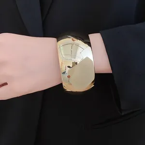 Macro detail view of a wide chunky gold metallic cuff bracelet worn on a female wrist