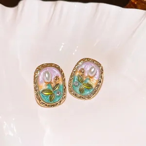 Close-up of vintage enamel tulip earrings with pearls and crystal accents on white shell