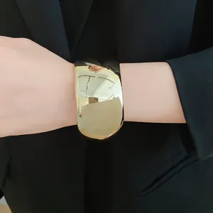 Close-up of a chunky gold geometric cuff bracelet worn over a black blazer sleeve.