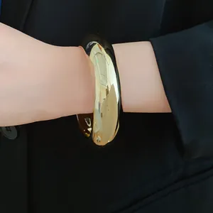 Detail shot of a chunky gold acrylic geometric bangle worn over a black blazer sleeve.