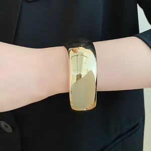 Detailed shot of a wide polished gold cuff bracelet worn on a wrist over a dark blazer