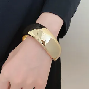 Close-up of a wide chunky gold geometric acrylic bangle worn on a wrist.