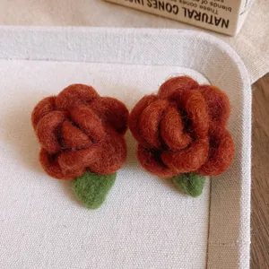 Dettaglio di orecchini fatti a mano in feltro di lana con fiori rossi e foglie verdi