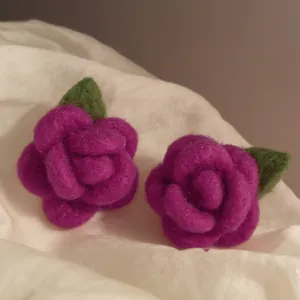 Dettaglio di orecchini a lobo a forma di rosa floccata viola con foglie verdi su tessuto