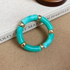 Detail view of teal marbled acrylic bracelet with gold-tone spacers resting on a vintage book