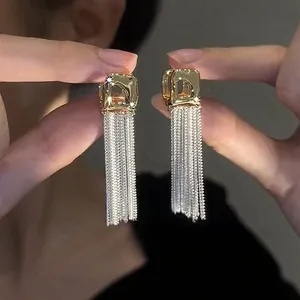Detailed macro view of gold square stud earrings with long flowing silver chain tassels