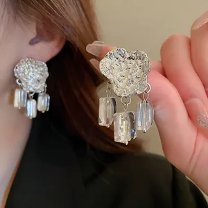 Macro detail of silver hammered metal stud earrings with three clear rectangular crystal dangles.