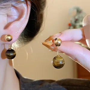 Detailed view of a model showing the texture of tiger eye stone drop earrings in hand