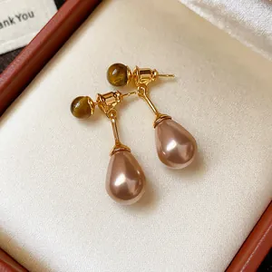 Close-up view of vintage Maillard style drop earrings with tiger eye stone and teardrop pearl