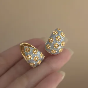 Detailed macro view of vintage gold C-shaped earrings with delicate flower enamel patterns