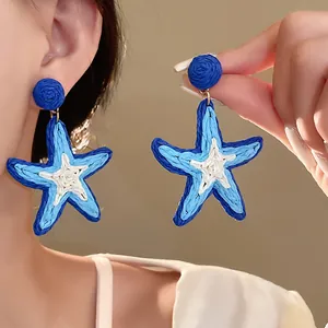 Detailed view of blue and white woven starfish earrings for a seaside holiday look.