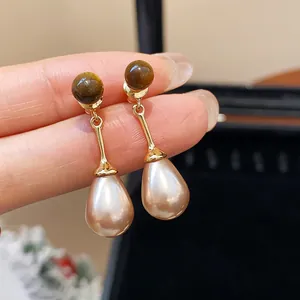 Detailed macro close-up of elegant vintage tiger eye and teardrop pearl drop earrings.