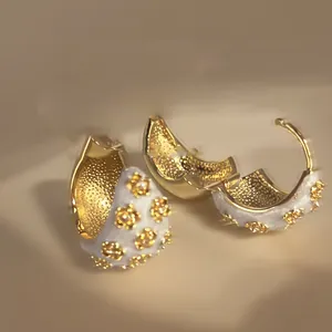 Macro view of C-shaped gold hoop earrings with white dripping oil enamel flower detailing