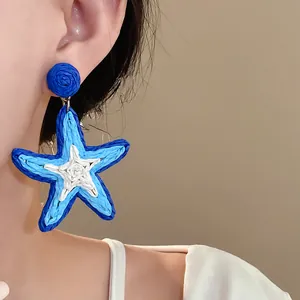 A detailed close-up shot of blue and white woven raffia star earrings on a model's ear