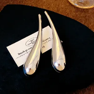 Dettaglio macro di grandi orecchini a goccia in argento lucido su sfondo nero.