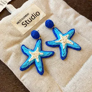 Macro view of blue woven starfish drop earrings with white center on textured pouch