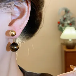 Close-up of gold-plated tiger's eye ball earrings on ear in warm indoor setting